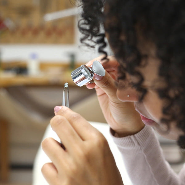 Person using tweezers and loupe to examine jewelry detail.