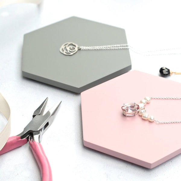 A silver necklace with a rose pendant and pink gemstone necklace on coasters, plus jewelry pliers.